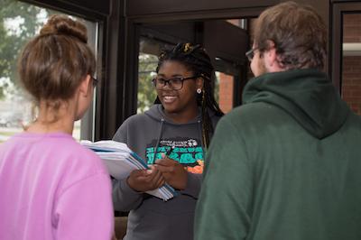 A student holding a notebook and interviewing two other students